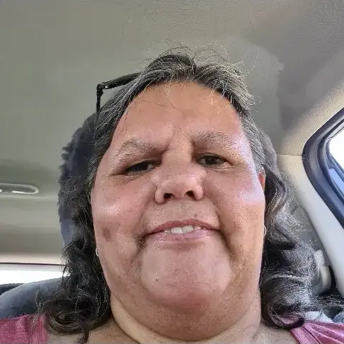 Portrait of Janelle with curly hair, wearing a pink top, seated in a car.