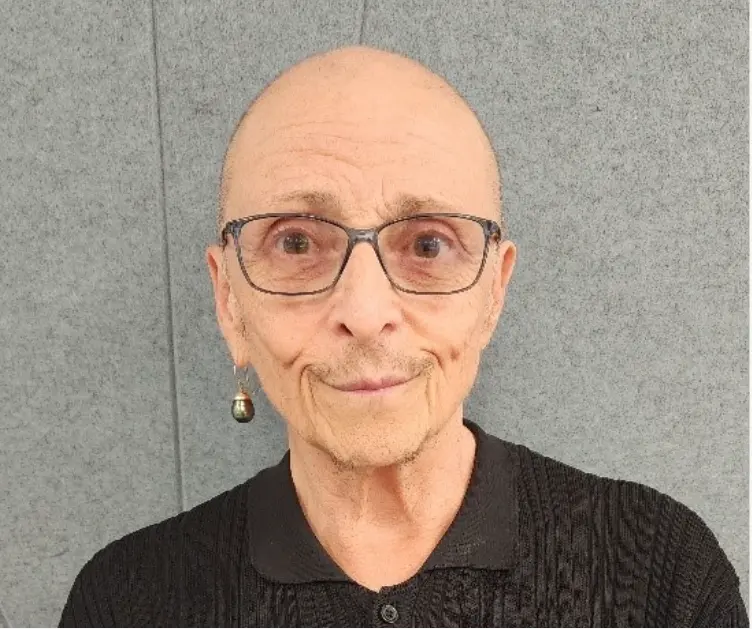 Sujay smiles in front of a grey wall, wearing a black top and an earring in the right ear.