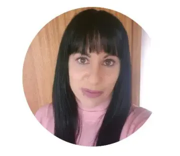 Portrait of Tess with long dark hair and bangs, wearing a pink top, against a wooden background.